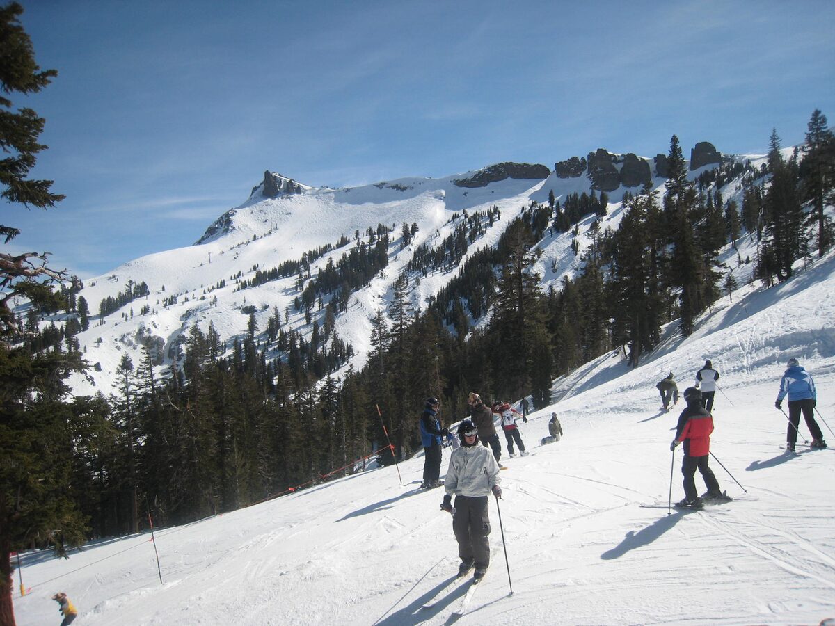 Skiers on a groomed run at Kirkwood, with a rocky ridge and pines above