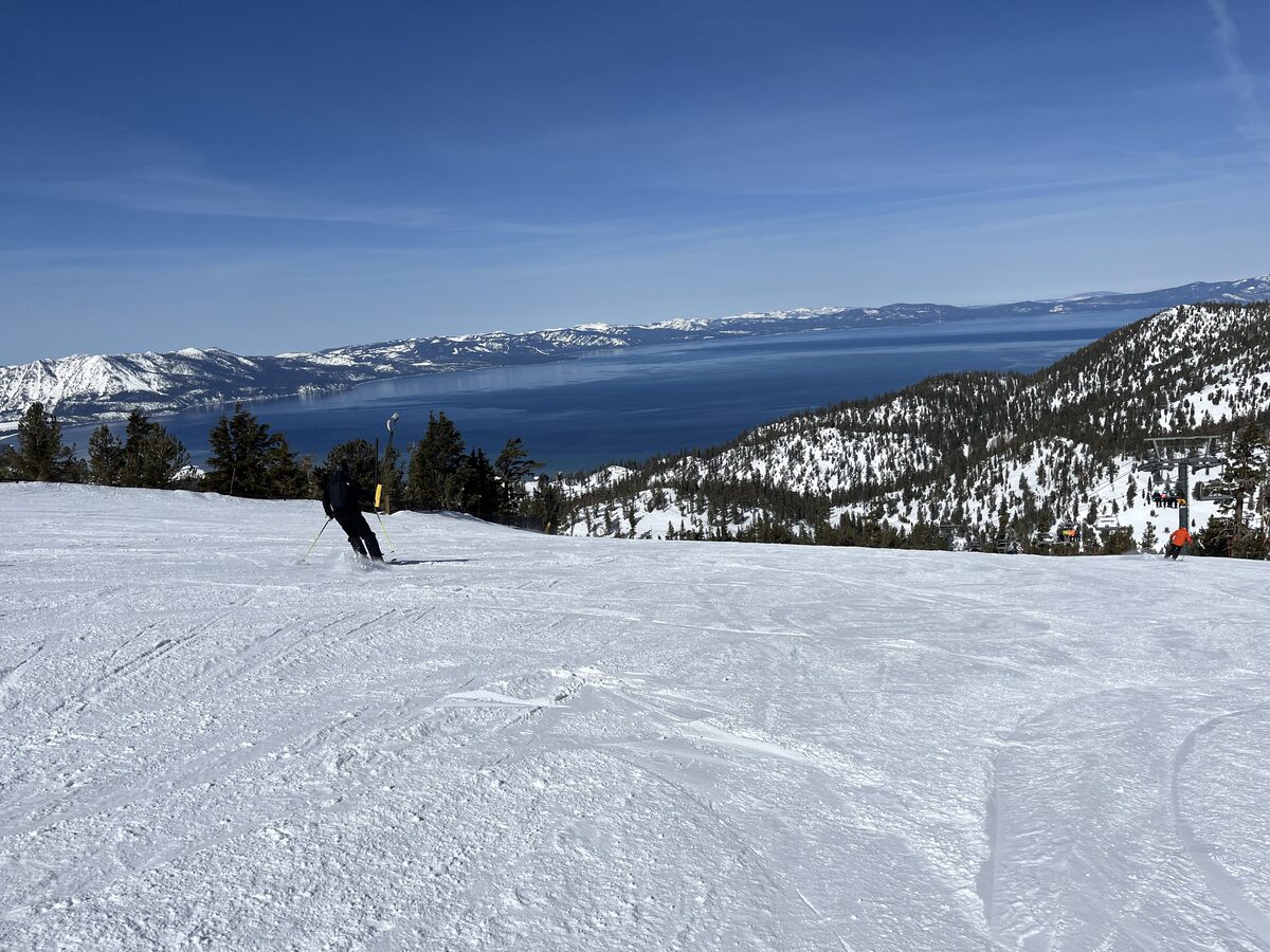 A skier on a wide snowy run high on Heavenly, with Lake Tahoe and the Sierra crest beyond