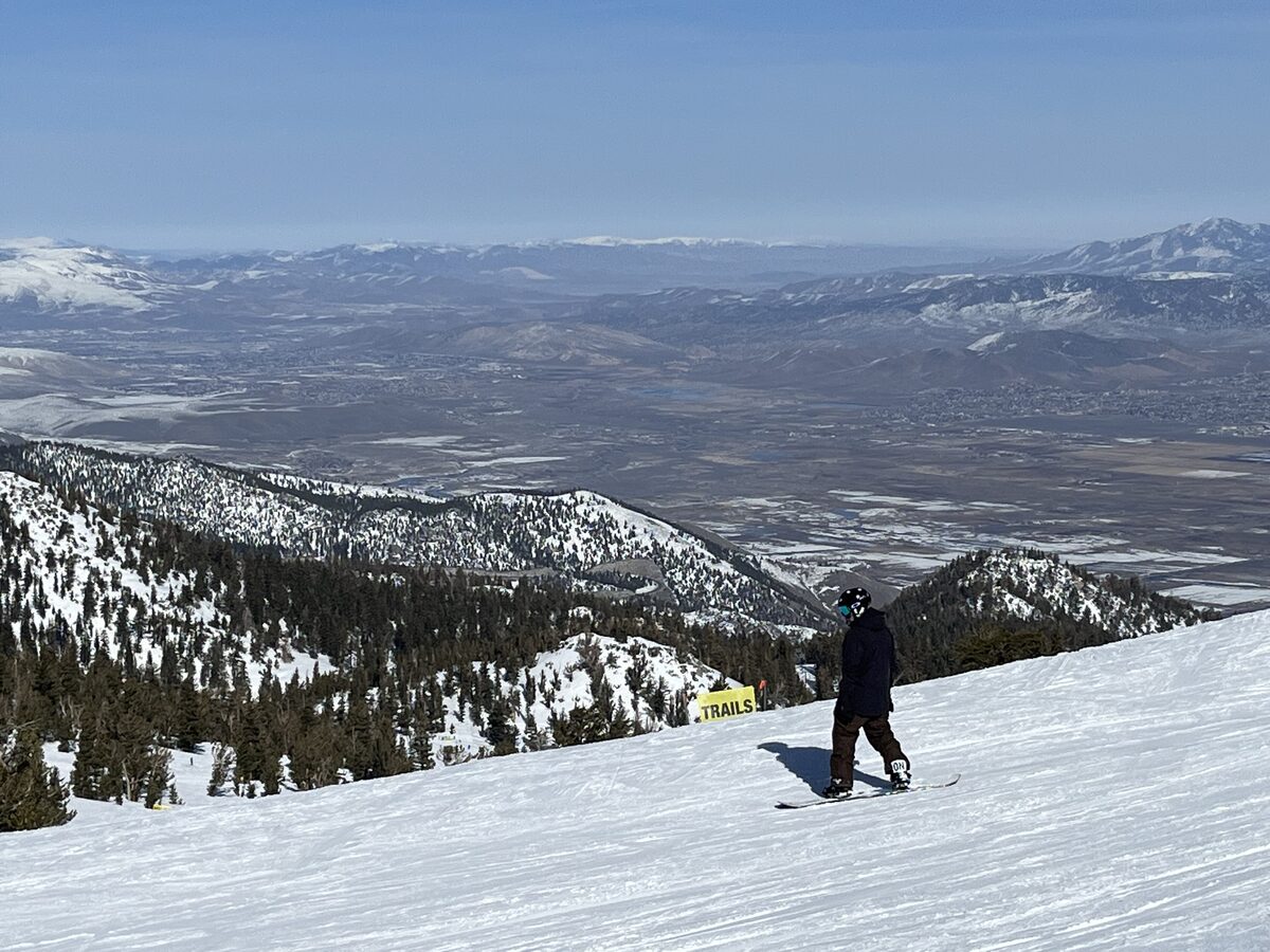 A snowboarder on a wide groomed run on Heavenly's Nevada side, looking east over the desert valley and ranges below