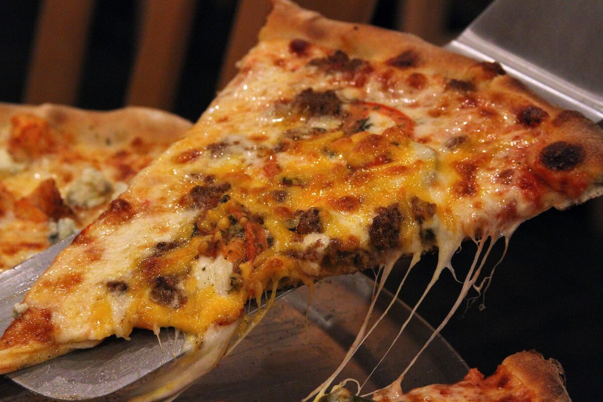 A cheesy slice of New York-style pizza lifted on a spatula
