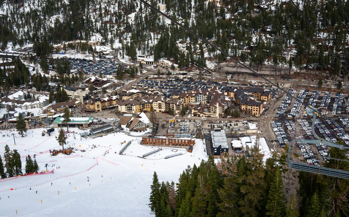 Aerial view of the snow-covered Palisades Tahoe village, with a ski run and parked cars