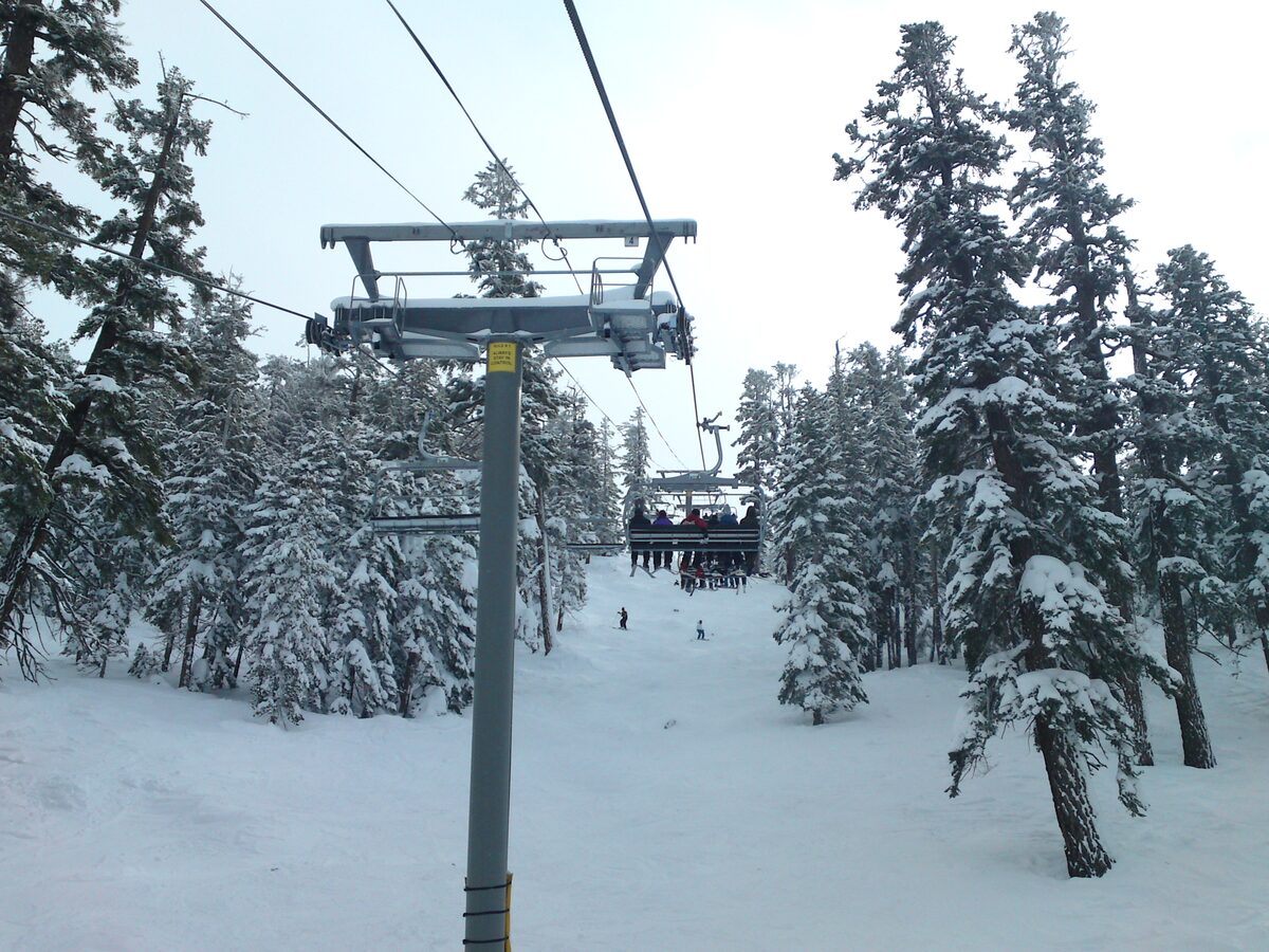 A chairlift running through snow-covered pines, with skiers on the slope below