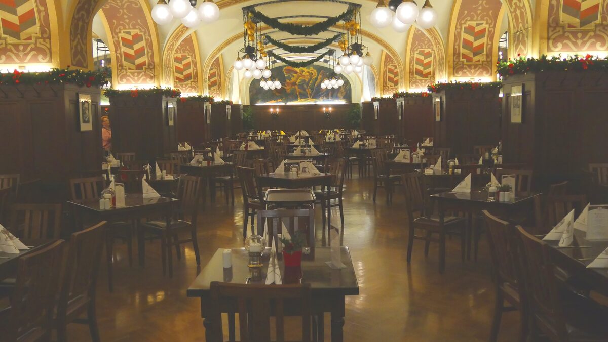 A vaulted, painted dining hall in Auerbachs Keller, with rows of laid tables and wreaths hanging from the ceiling