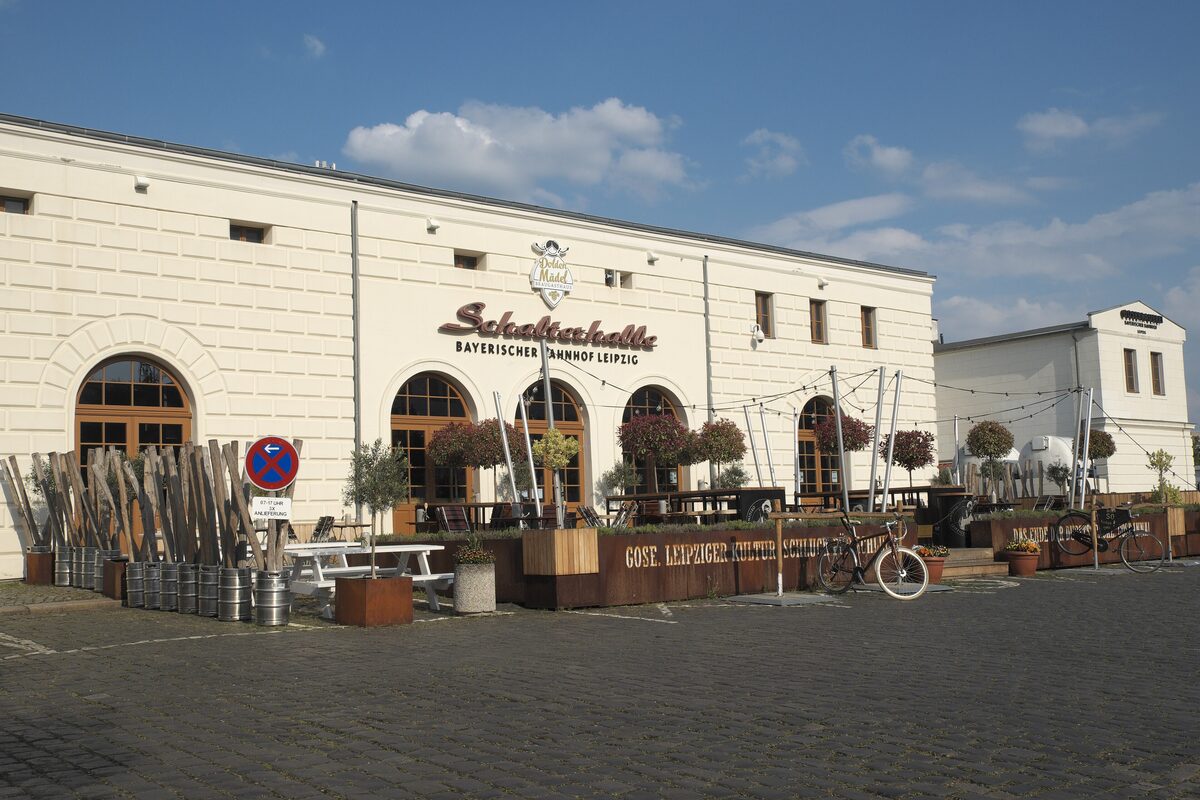 The cream-colored Bayerischer Bahnhof building with the brewery's terrace, tables and arched windows