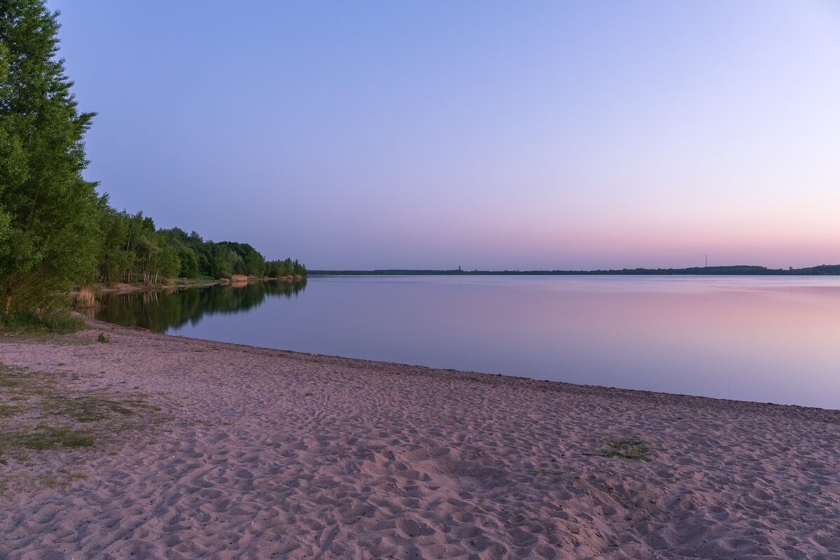 A sandy beach on the Cospudener See at dusk, with the water and sky turning pink