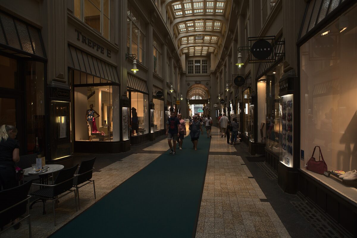 Looking down the Mädlerpassage, a long glass-roofed arcade with lit shop windows and café tables