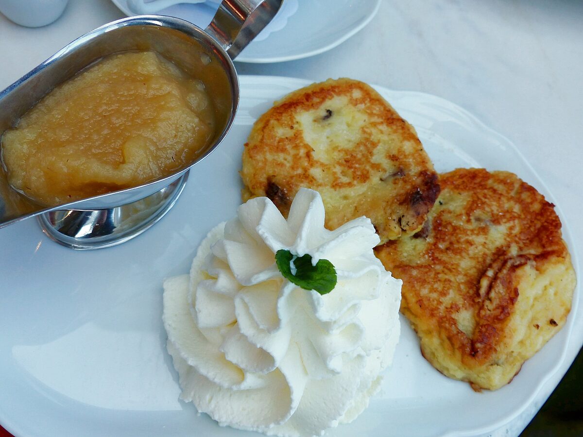 Two golden quark and potato pancakes with apple sauce and a swirl of whipped cream