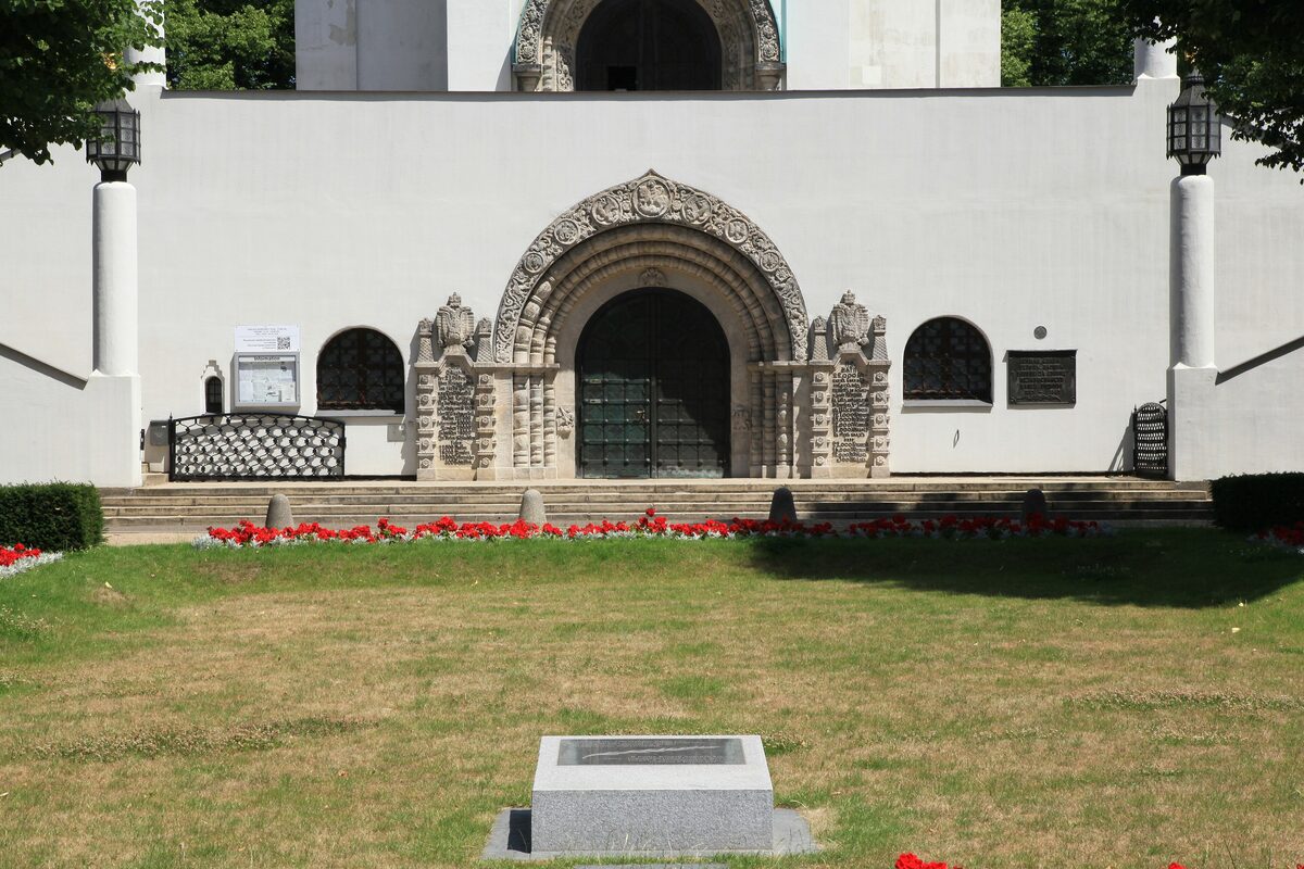 The arched stone portal of the Russian Memorial Church, set in a white wall above a lawn with red flowers