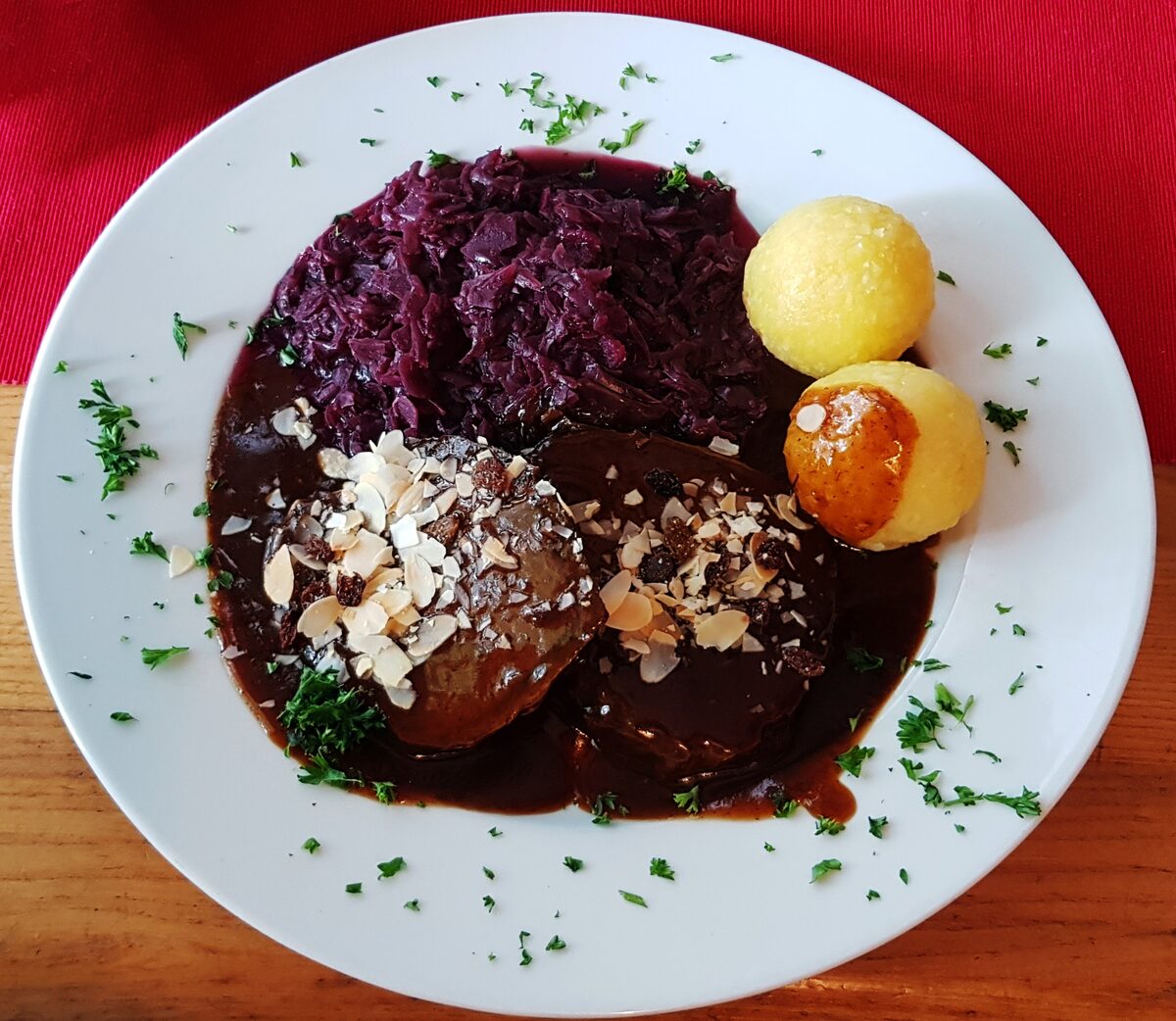 Sauerbraten in dark gravy with red cabbage and two potato dumplings on a white plate