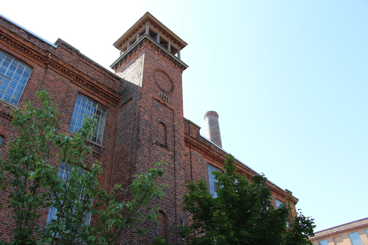 A brick tower and factory hall of the Baumwollspinnerei against a clear sky