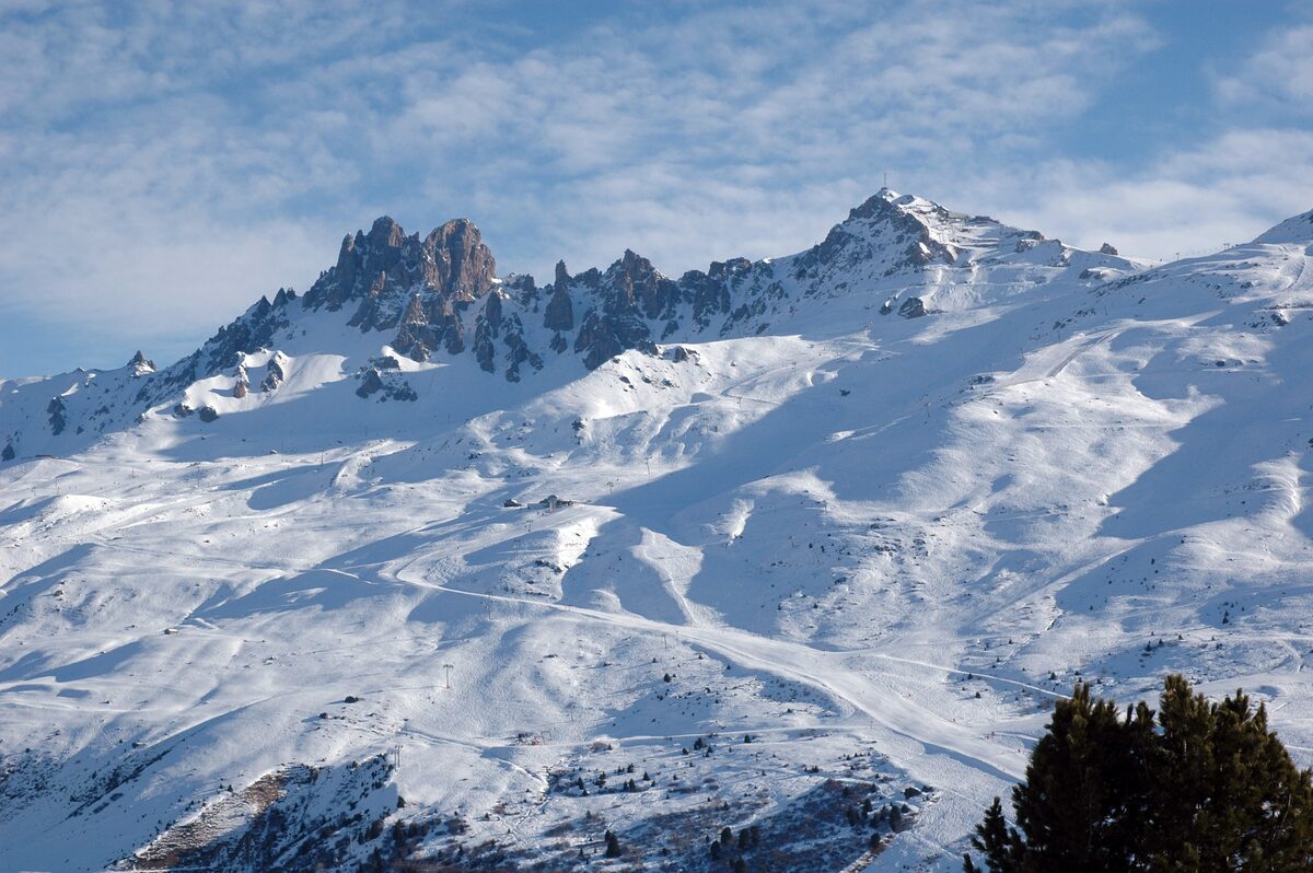 The jagged Dent de Burgin ridge and the Saulire summit above sunlit snowfields and pistes under a blue sky
