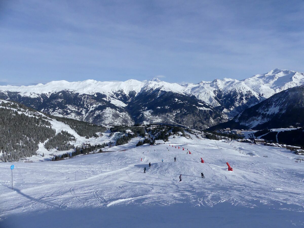 Skiers on a wide snowy piste above Courchevel 1850, with the mountains behind
