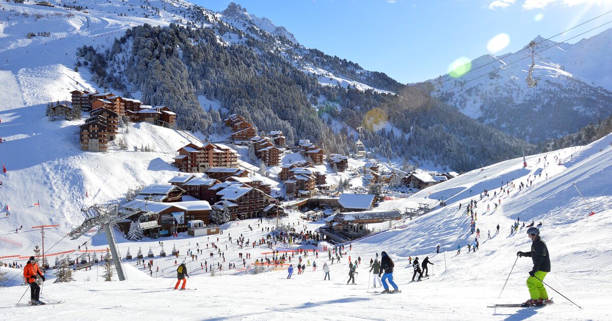 Skiers on the snowfront of Méribel-Mottaret, with timber chalets, pine forest and snowy peaks behind