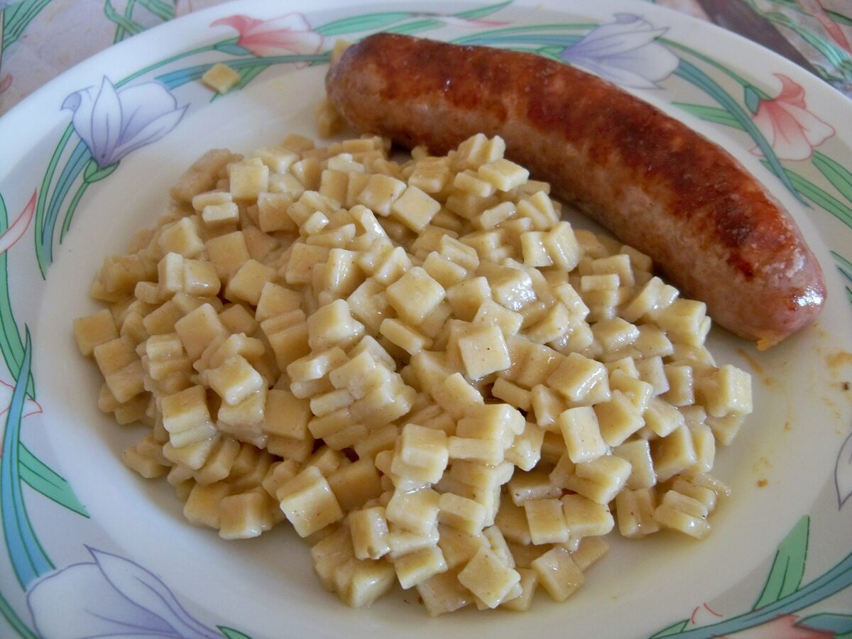 A plate of cooked crozets, small squares of Savoyard pasta, served with a grilled sausage
