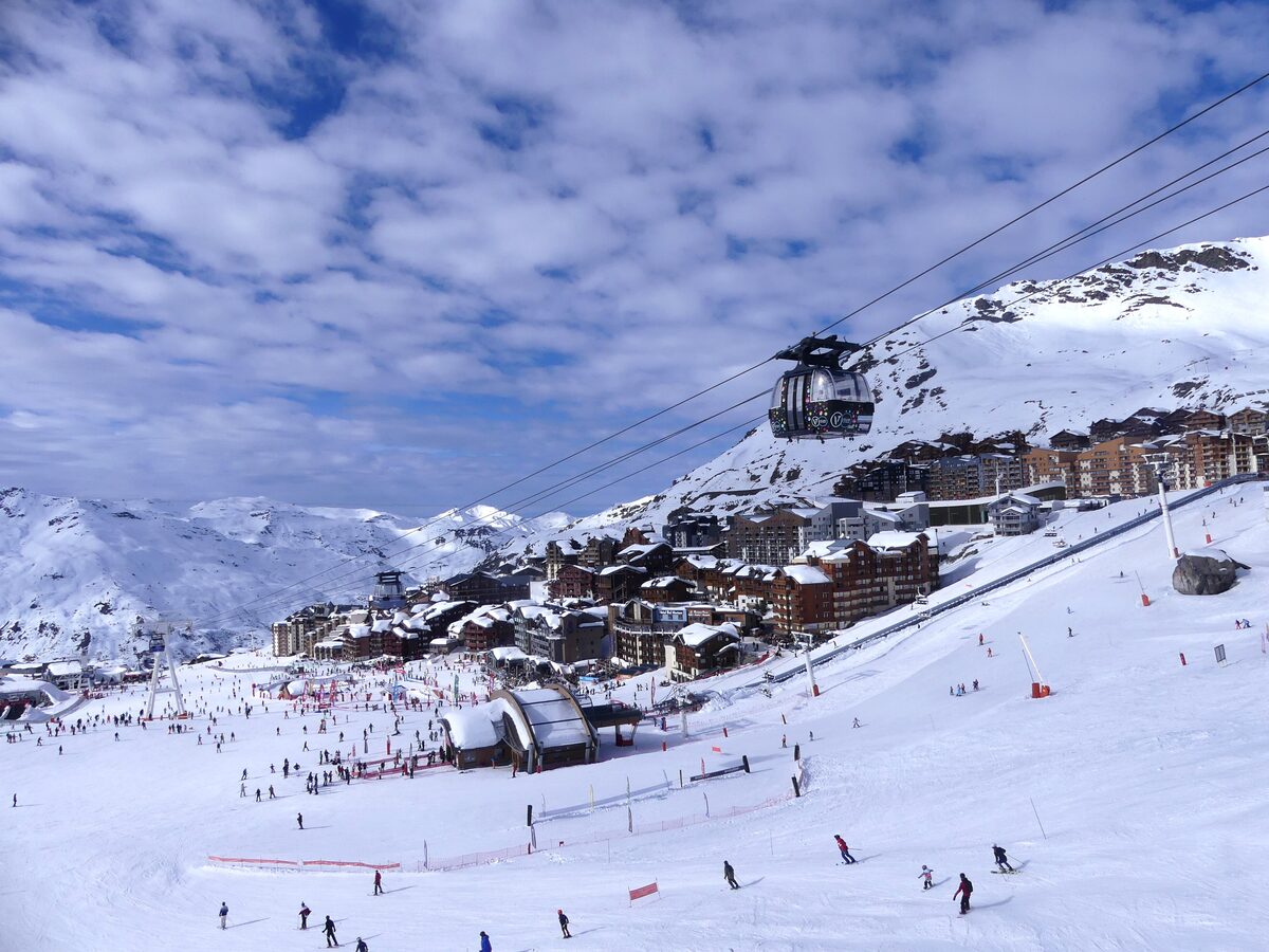 A funitel cabin on its cables above the busy snowfront of Val Thorens, with the village and snowy slopes beyond