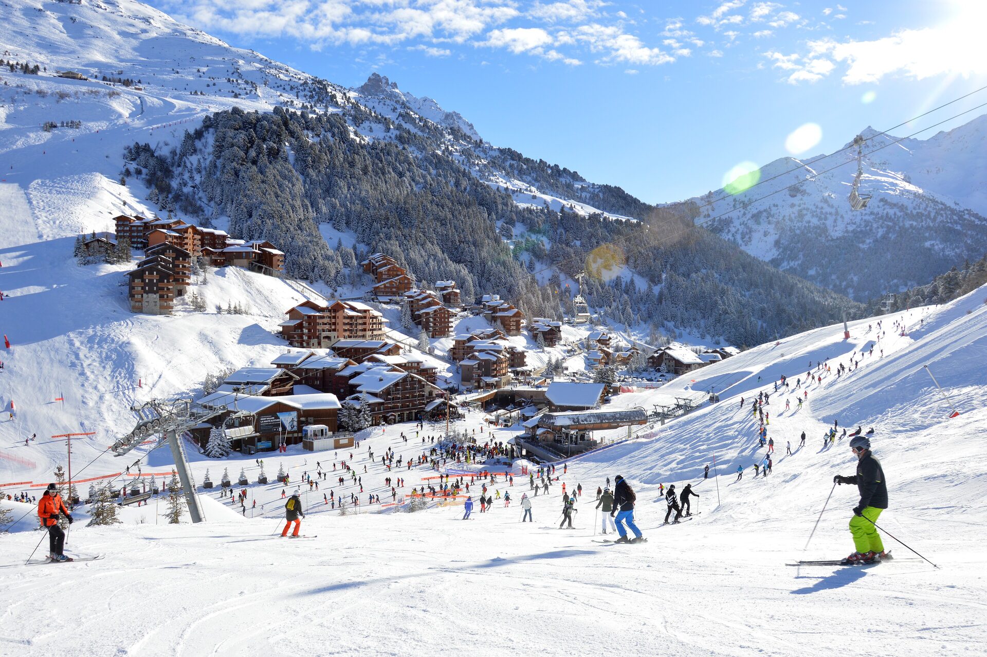 Skiers on the snowfront of Méribel-Mottaret, with timber chalets, pine forest and snowy peaks behind