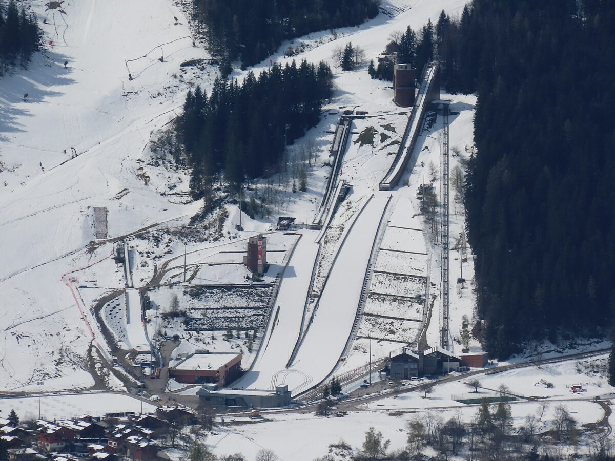 The Olympic ski jumps of Le Praz seen from above, snow-covered between dark conifer forest