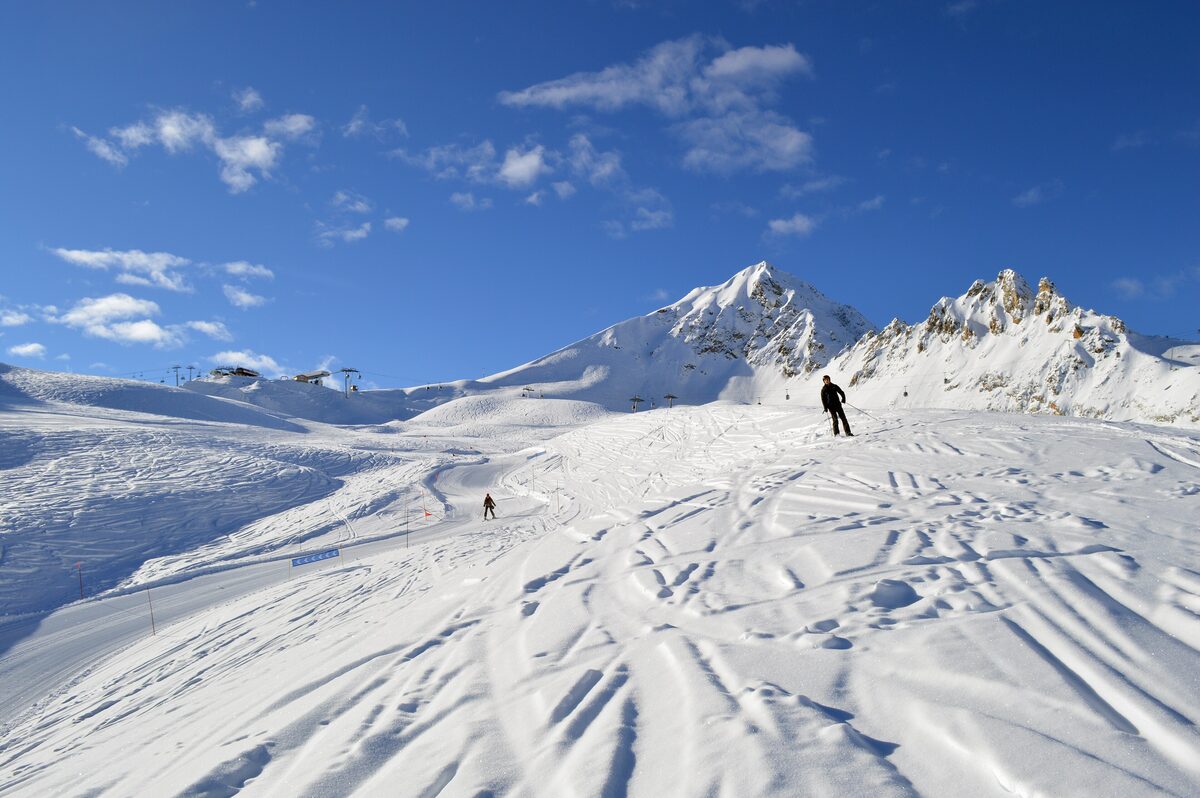 A wide, open snow slope at Les Arcs with a lone skier and a sharp peak beyond under a clear sky