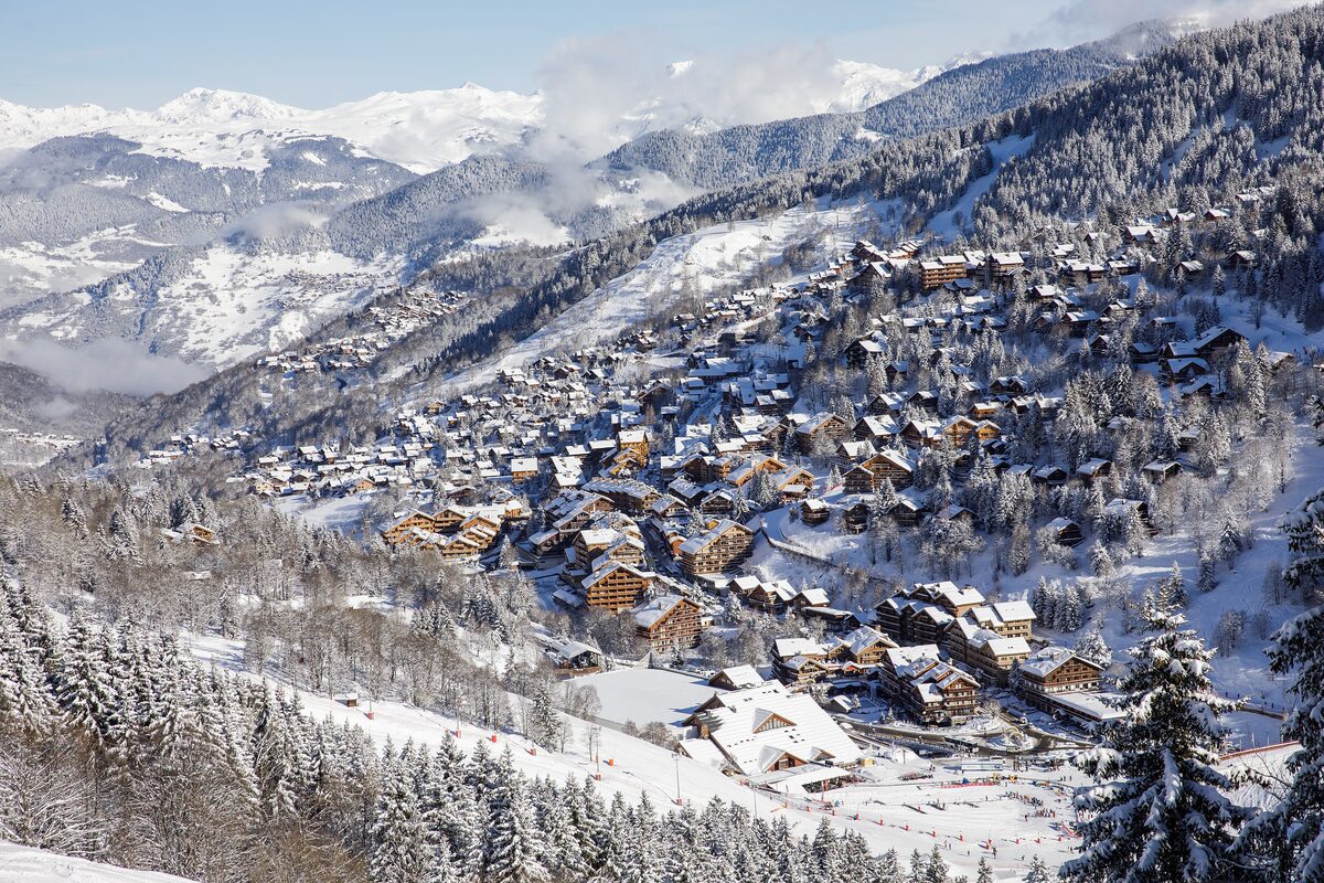 Snow-covered chalets of Méribel-Centre on the hillside, with pine trees and mountains behind
