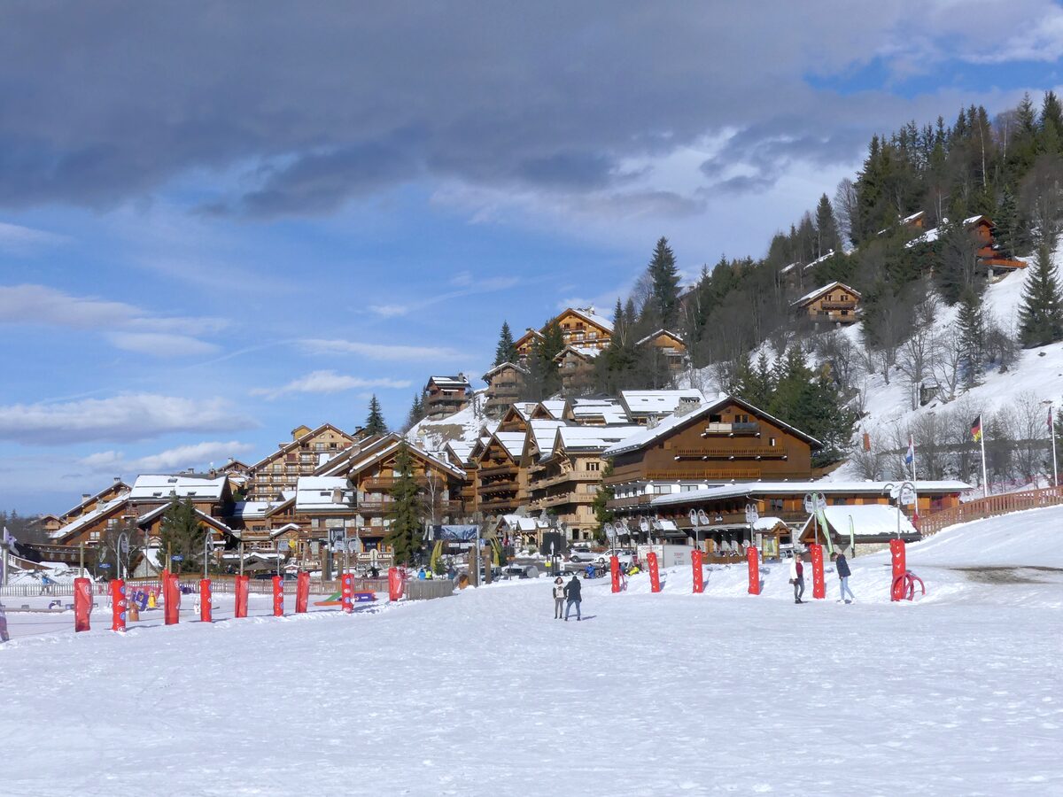 The snow-covered front of Méribel-Centre with timber chalets rising up the wooded hillside behind it