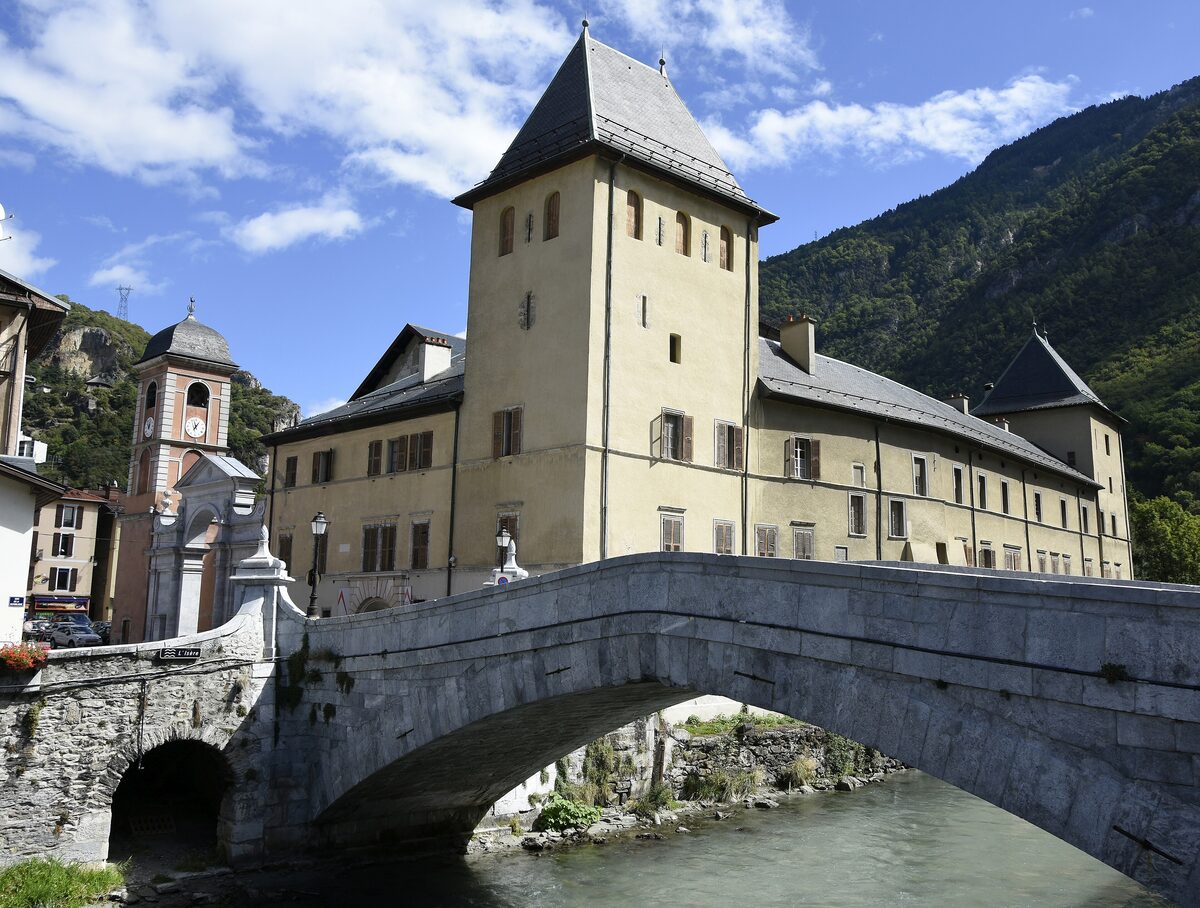 The old stone bridge over the Isère in Moûtiers with the former bishop's palace beside it under a blue sky