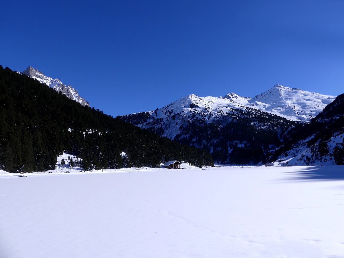 The frozen Lac de Tuéda under snow, with dark pine forest and peaks behind