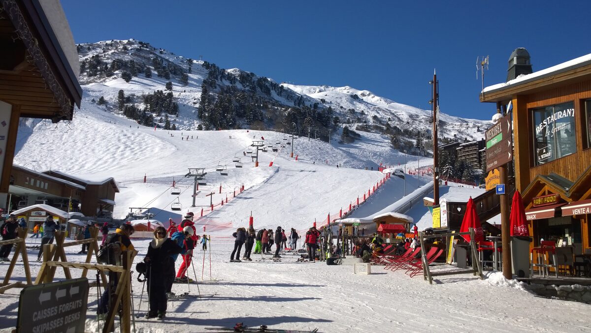 Skiers on the groomed piste at the Méribel-Mottaret ski departure, with chalets beside the snow