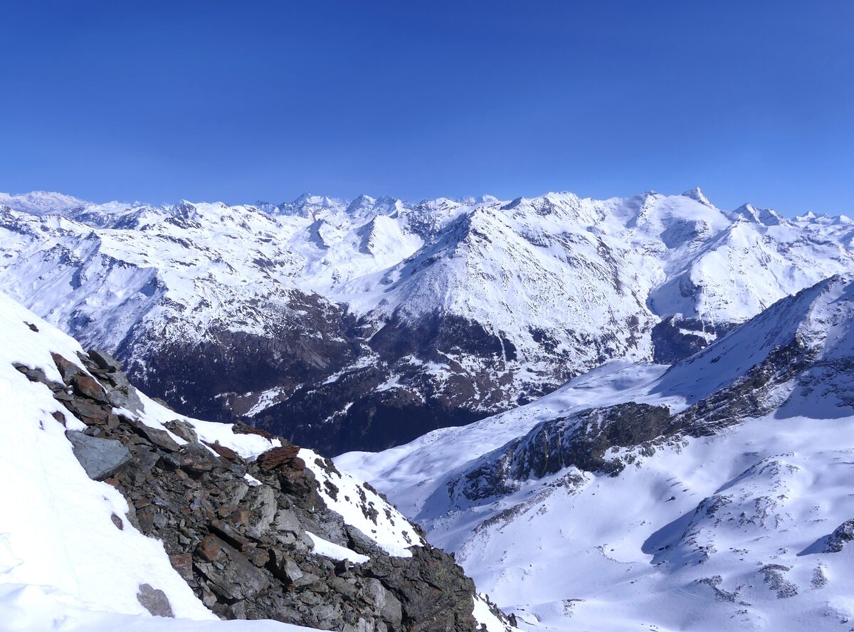 A view from the Aiguille Rouge summit ridge across snowy peaks under a blue winter sky