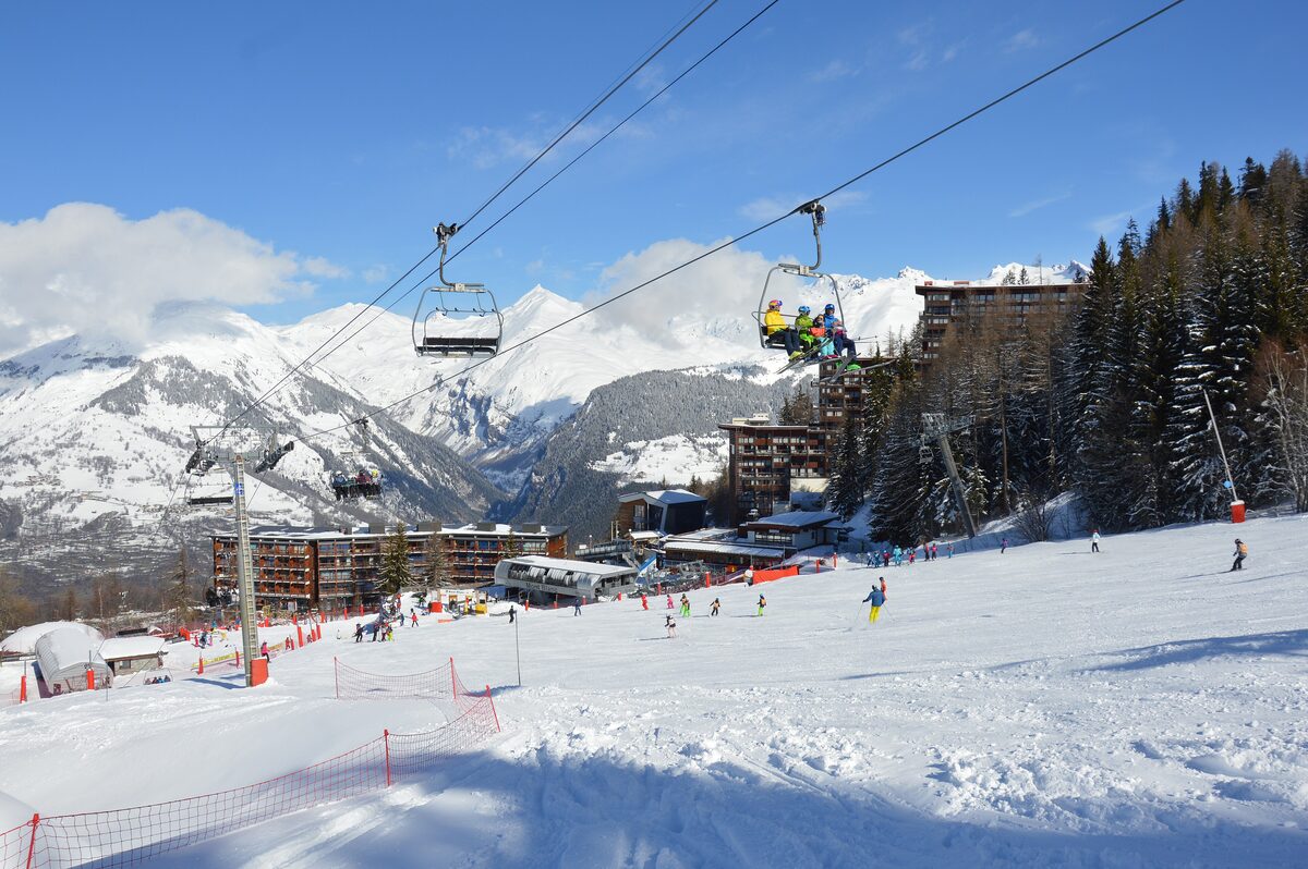 A chairlift and ski run above the snowy Arc 1600 village, with hotels on the edge of the pistes