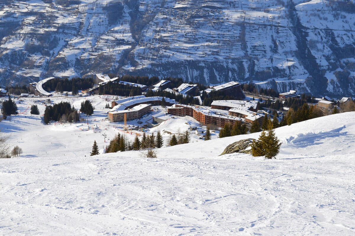 Ski runs and chalet roofs of Arc 1800 seen from above, with rocky mountains behind