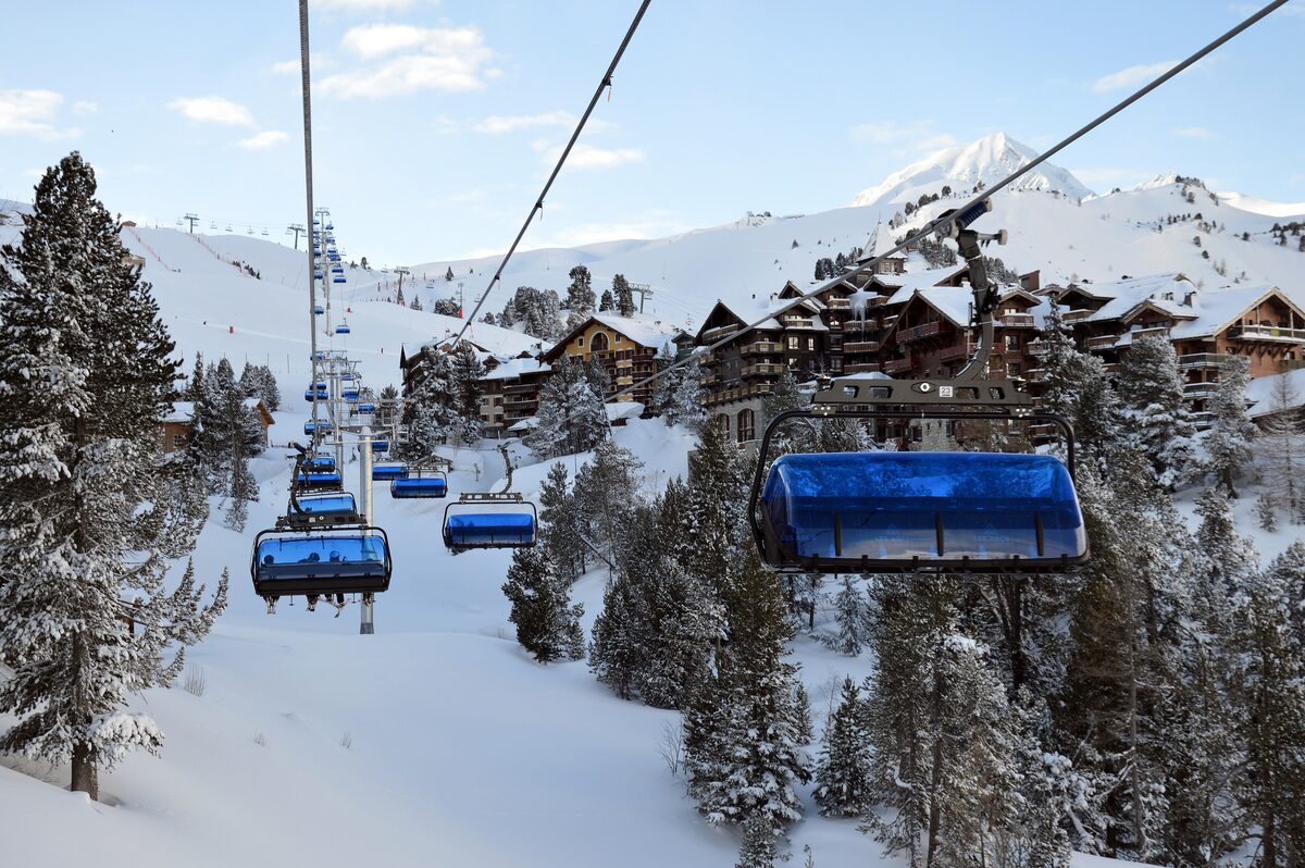 A chairlift over snowy trees, with the Arc 1950 chalets below and mountains beyond