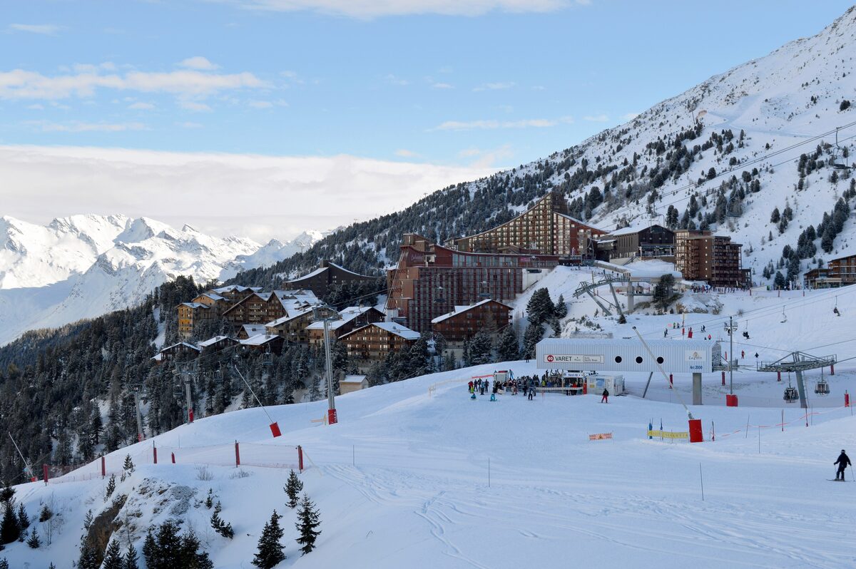 Hotels and skiers on the snowy Arc 2000 piste, with a chairlift running past the buildings