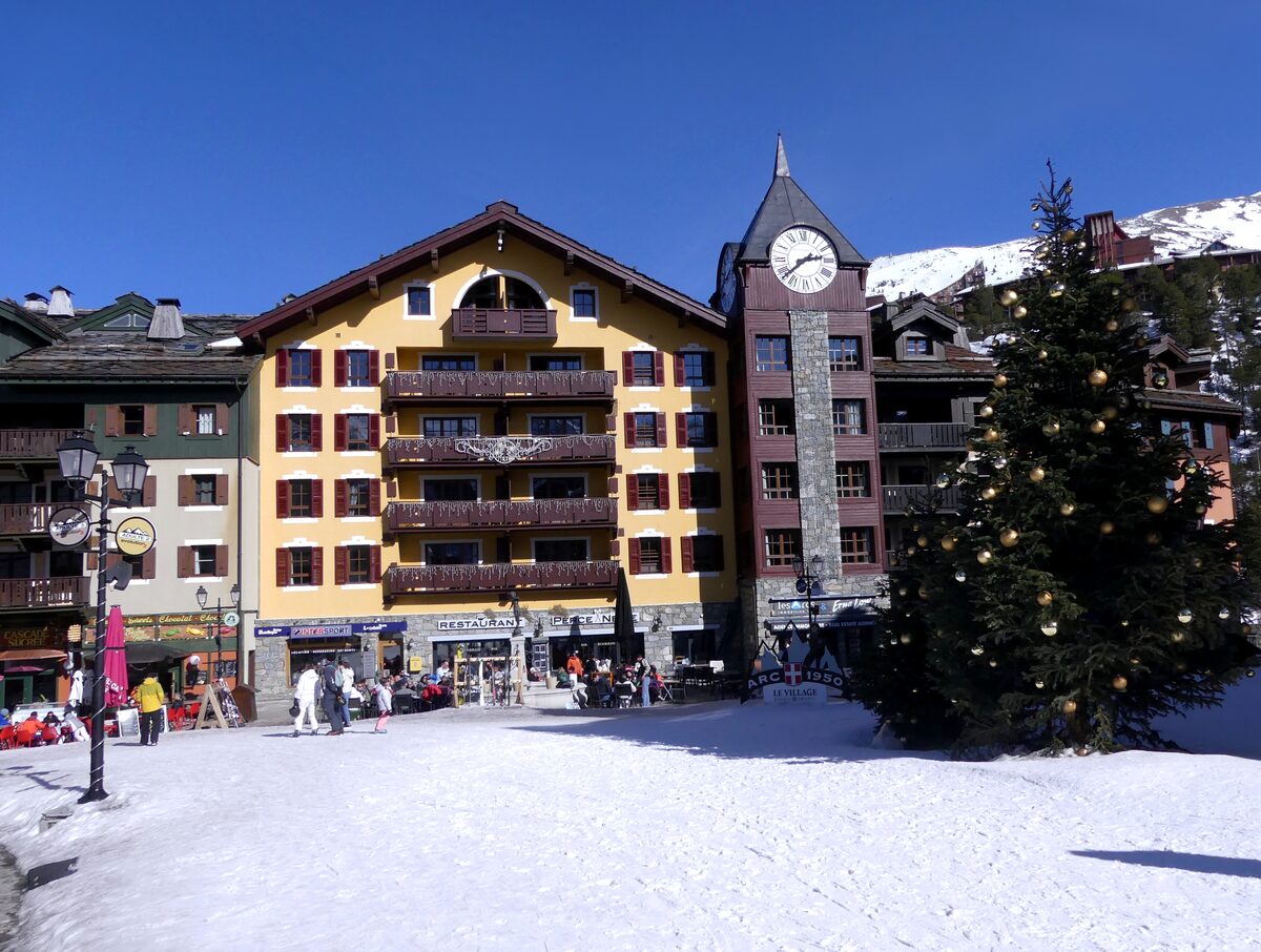 The clock tower and yellow chalets on the snowy village square of Arc 1950