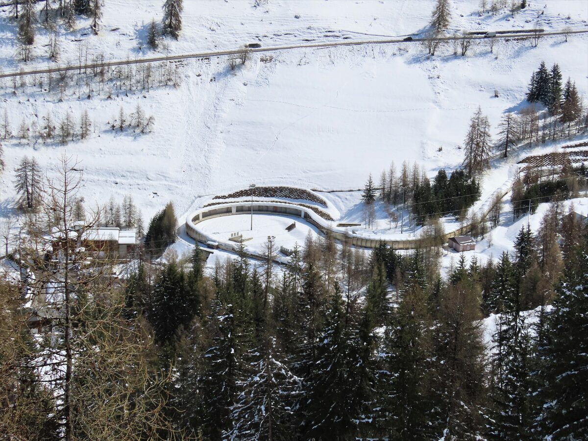 The curving La Plagne bobsleigh track in the snow, seen from above, with larch and spruce forest around it
