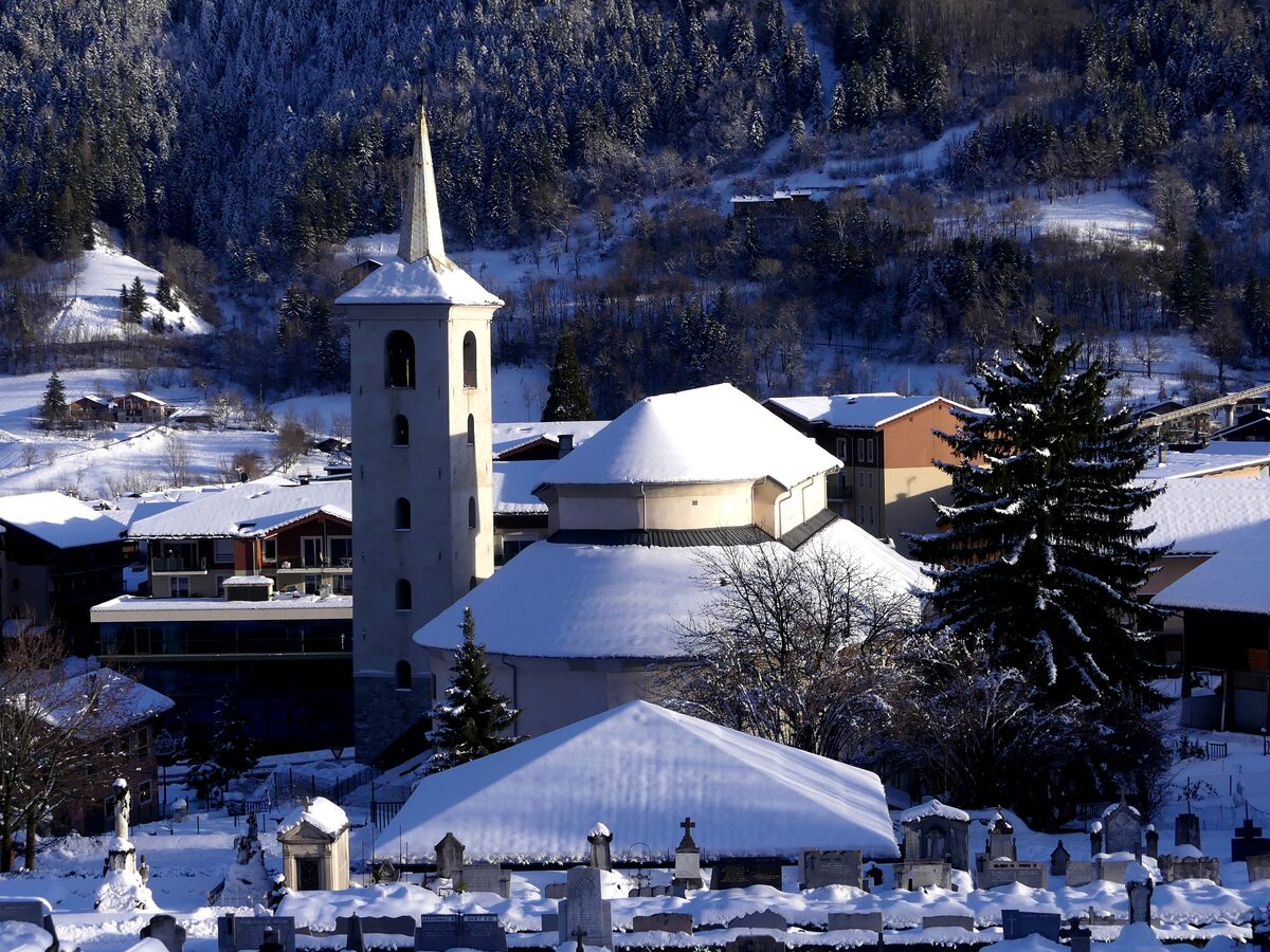 The snow-covered church tower and cemetery of Bourg-Saint-Maurice, with houses and a wooded slope behind