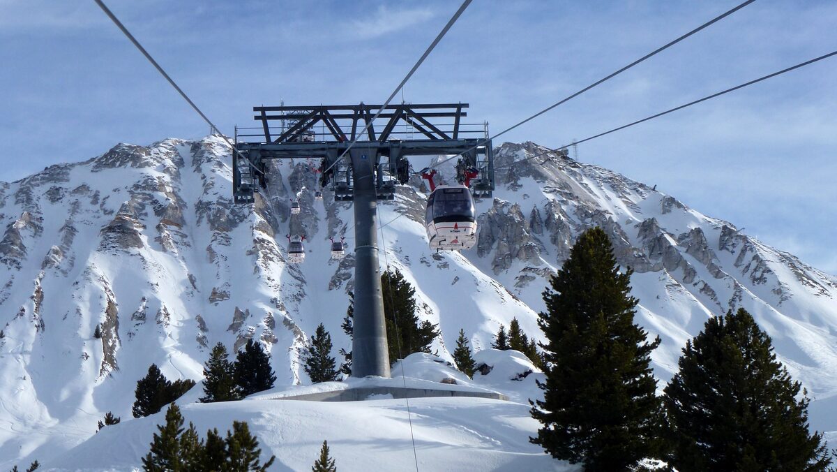 Funiplagne cabins passing a pylon below the rocky, snow-covered slopes above La Plagne