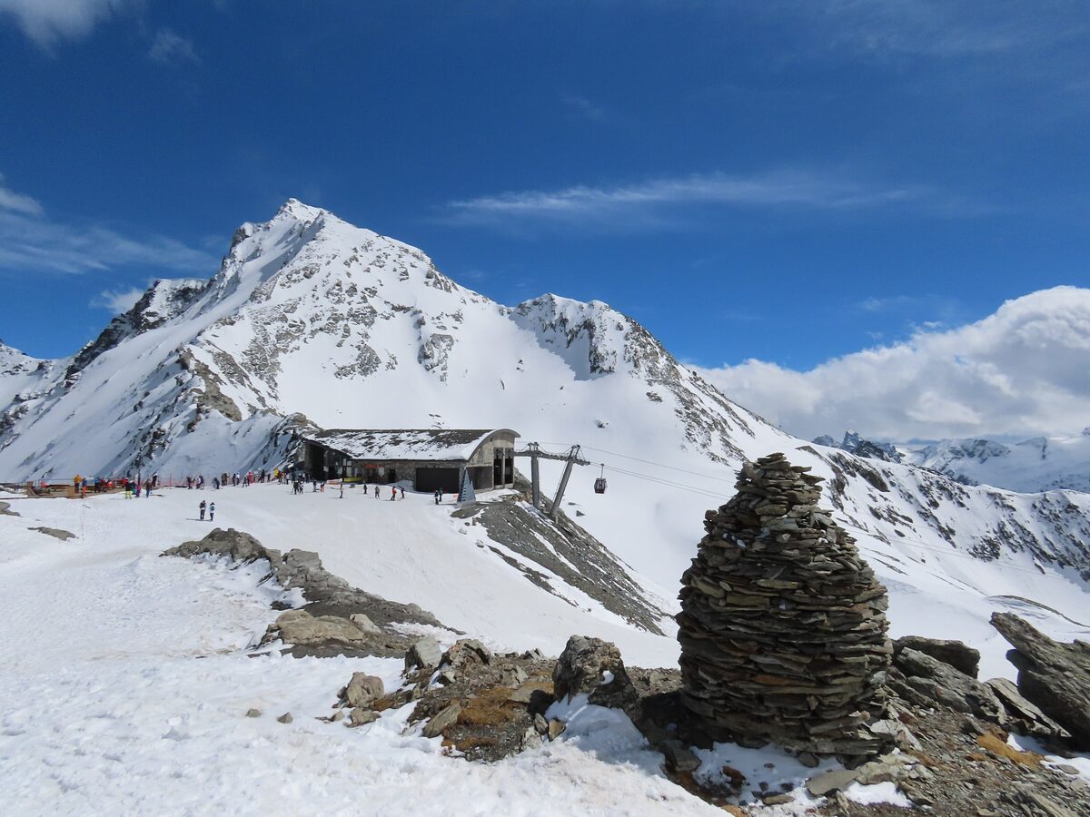 The top station of the Glaciers gondola at the Bellecôte glacier viewpoint, with a stone cairn and the snowy summit behind