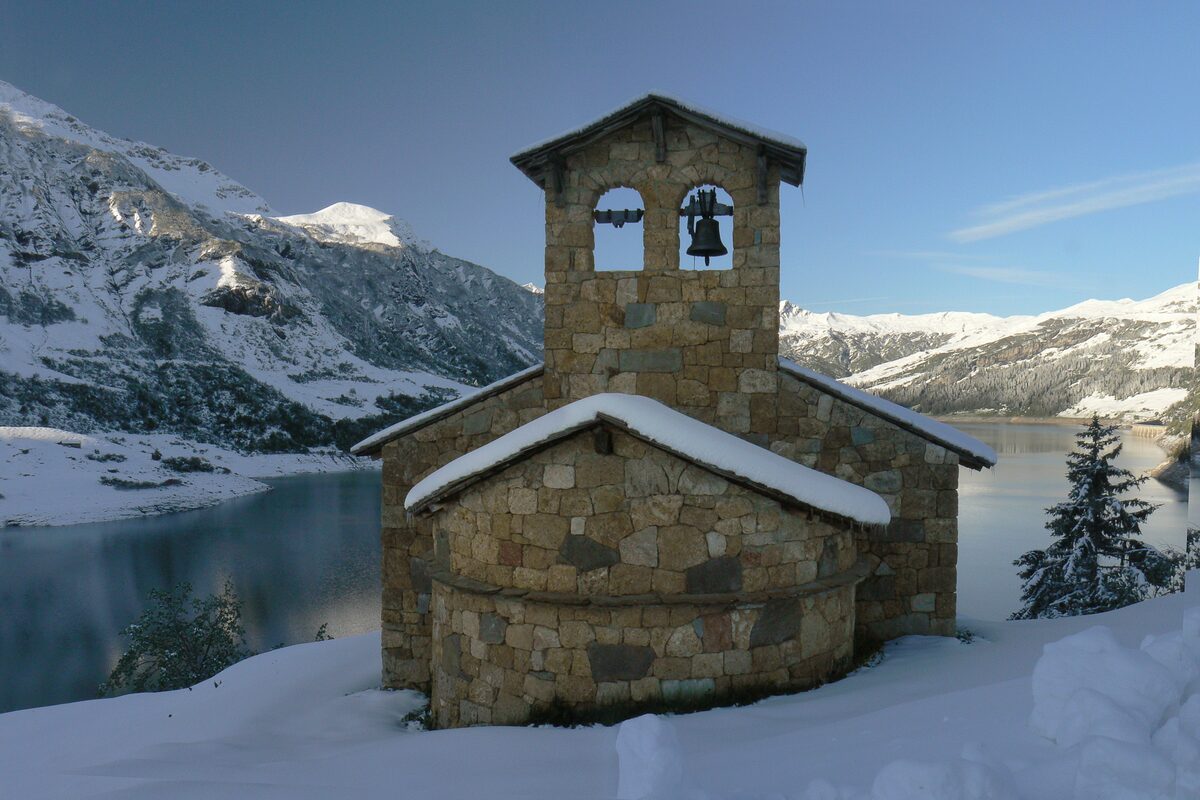 The stone chapel of Roselend in snow beside the reservoir, with snowy mountains behind