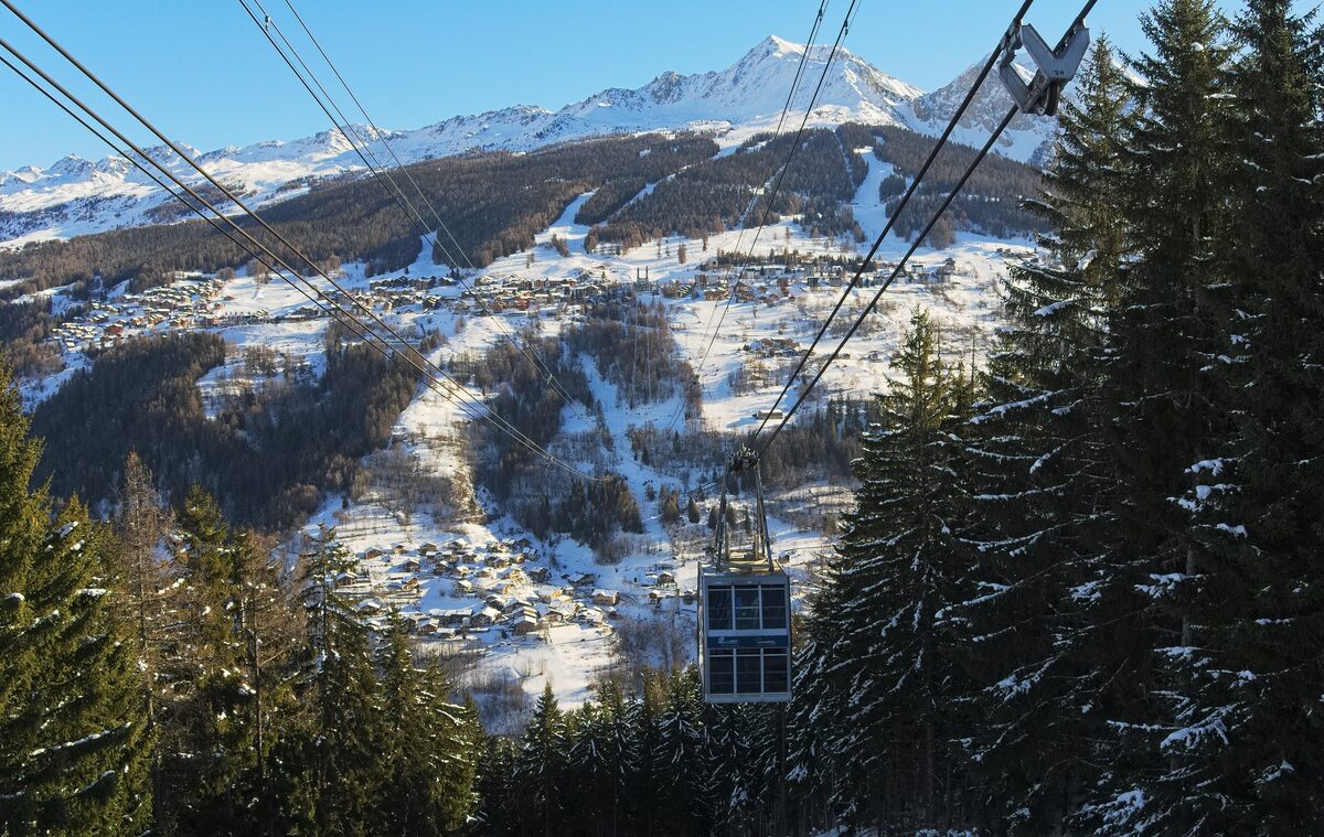 A Vanoise Express cabin hanging from its cables over snowy forest, with the Les Arcs side across the valley