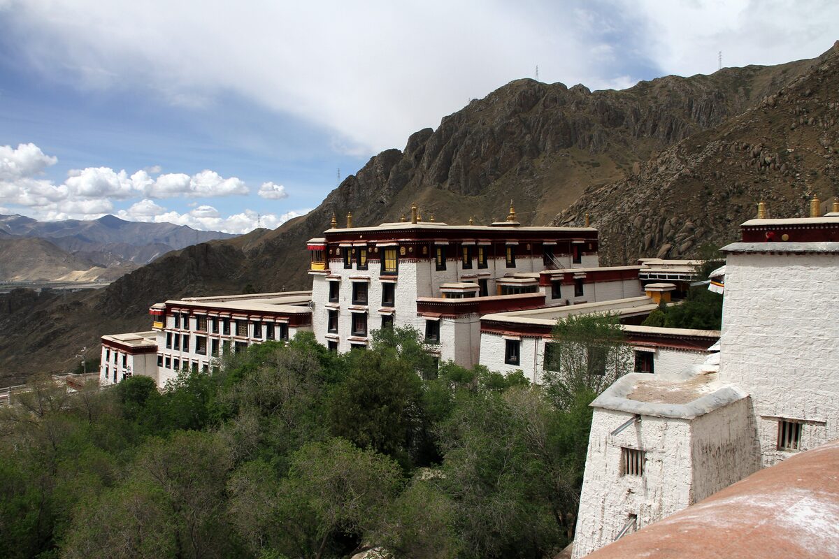 Whitewashed monastery buildings of Drepung climbing a dry mountain slope, with green trees and the Lhasa valley beyond