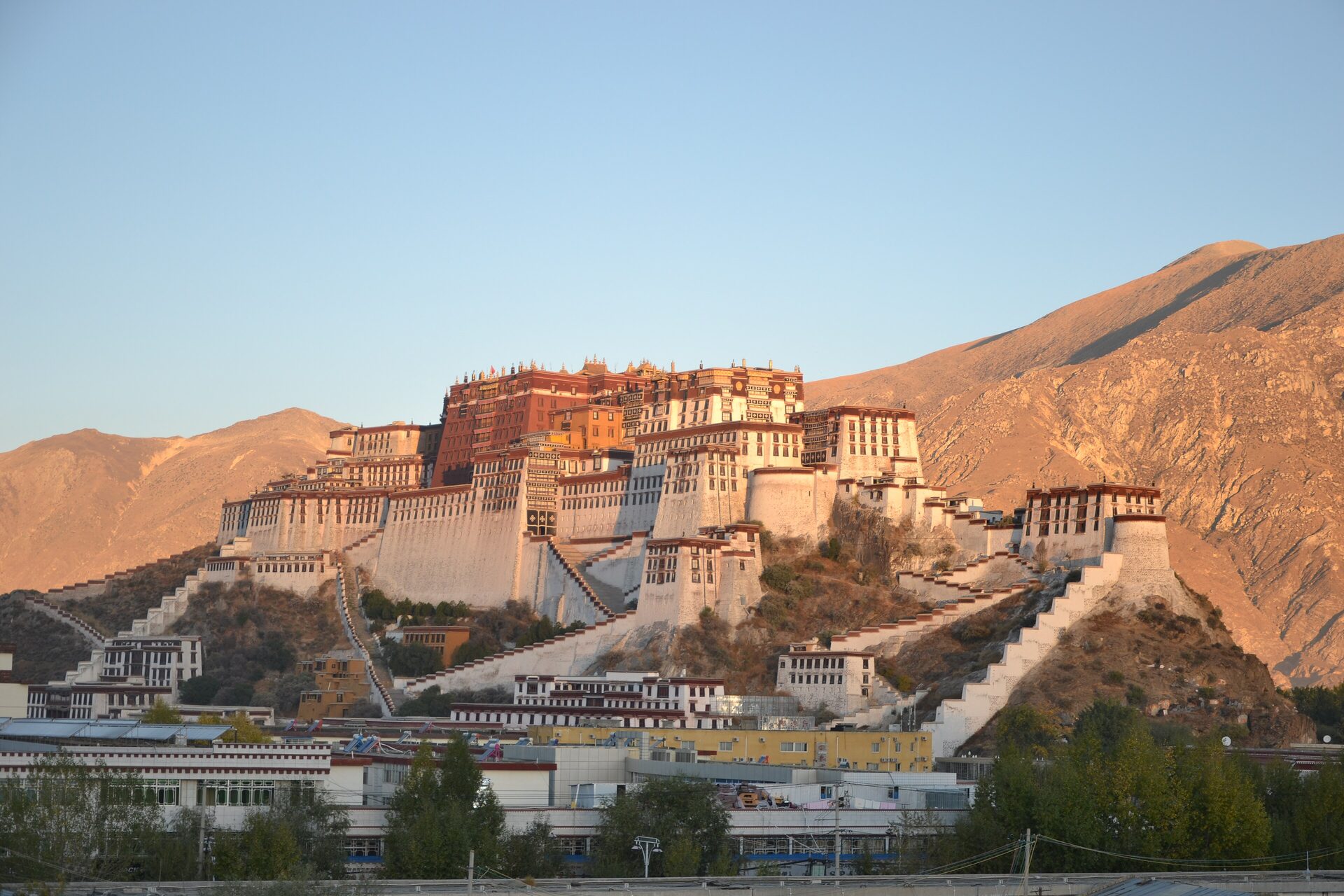 The Potala Palace, white and red walls on its hill in warm low sun under a clear sky, with bare brown mountains behind