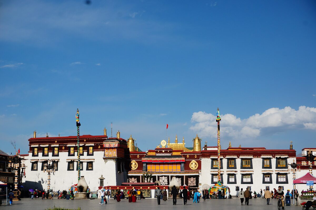 The front of the Jokhang with its golden roof ornaments and two tall flagpoles, seen across the open square