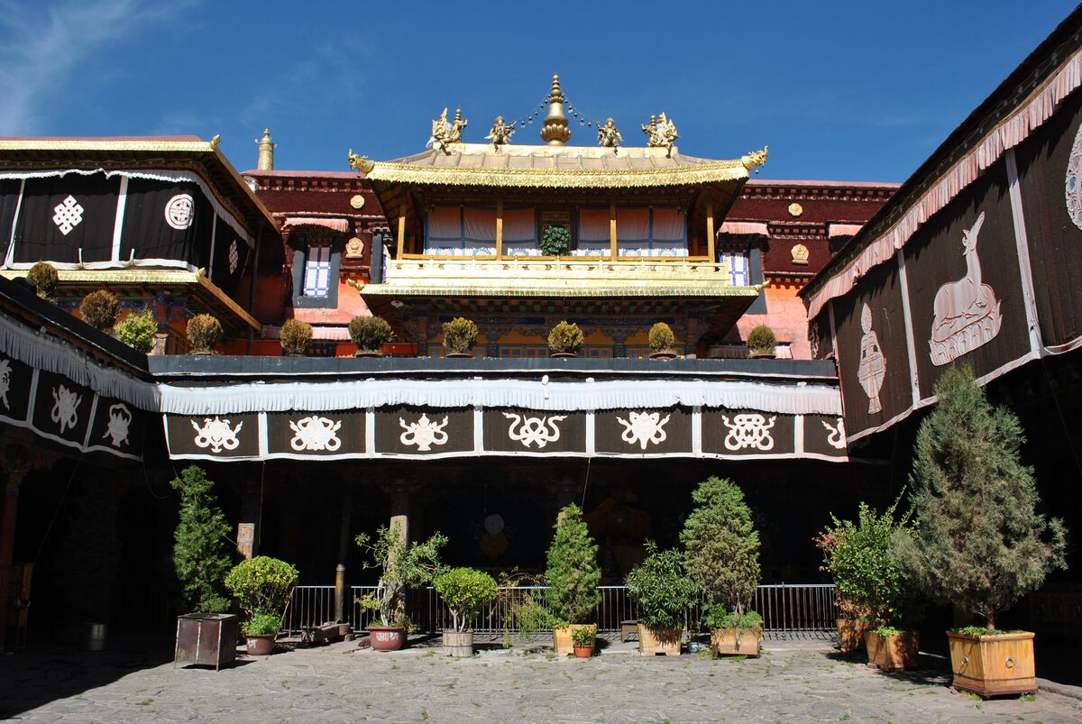 The inner courtyard of the Jokhang, with a gilded roof pavilion above black-and-white painted drapes and potted trees below