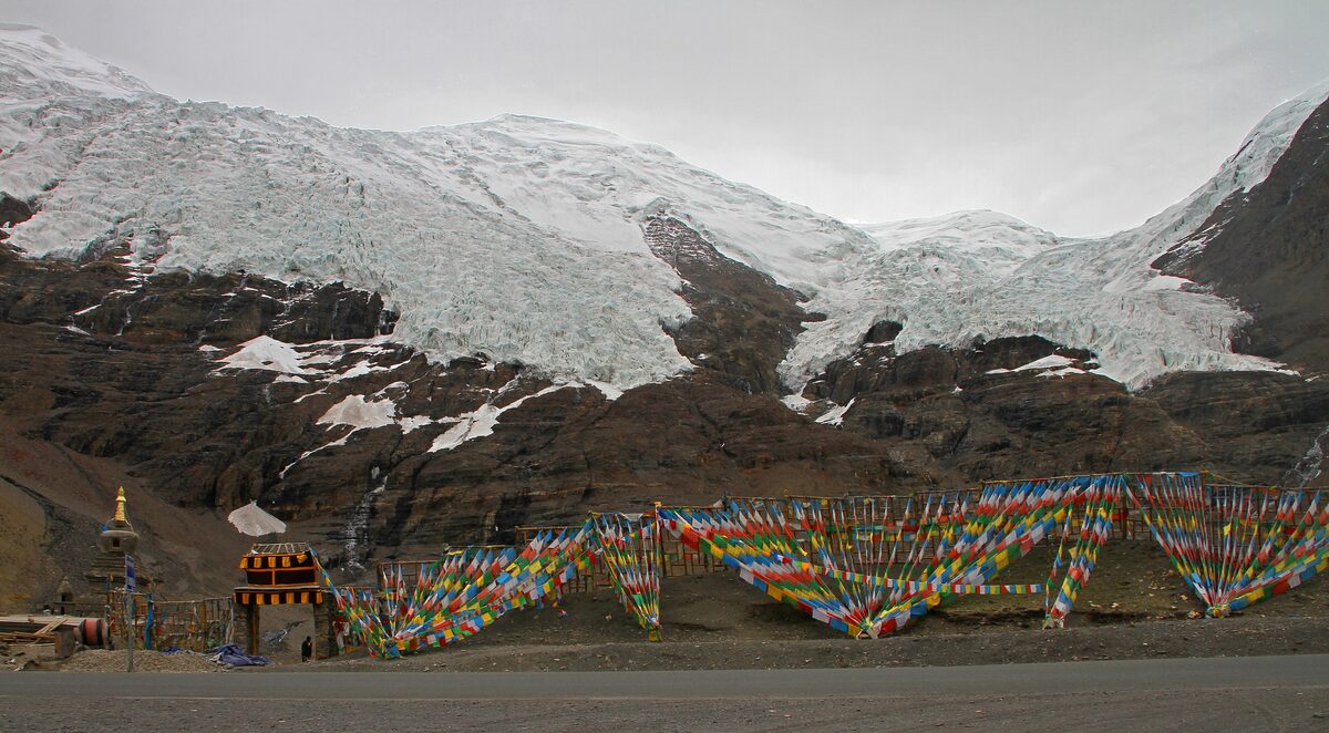 The Karola glacier hanging between dark mountain slopes above a line of colorful prayer flags