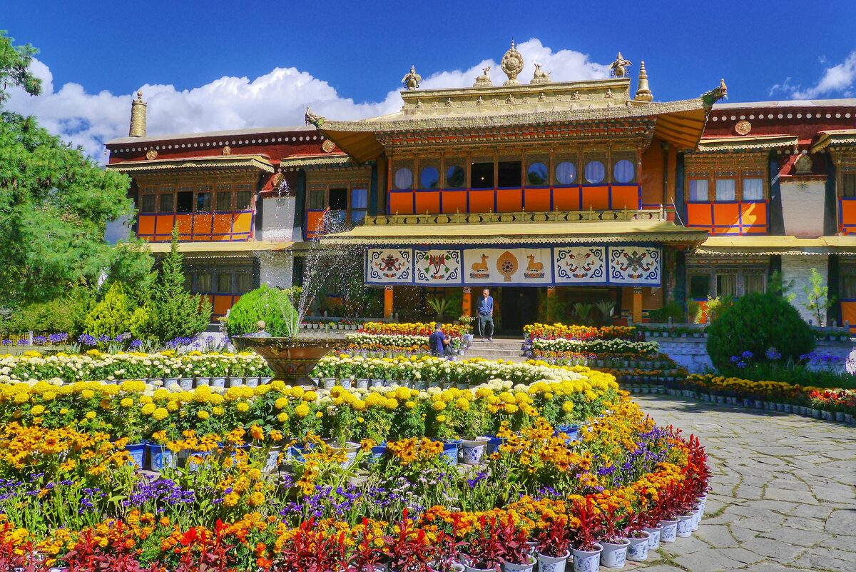 A palace at Norbulingka with a golden roof and painted wooden balconies behind a circular bed of yellow, red and purple flowers