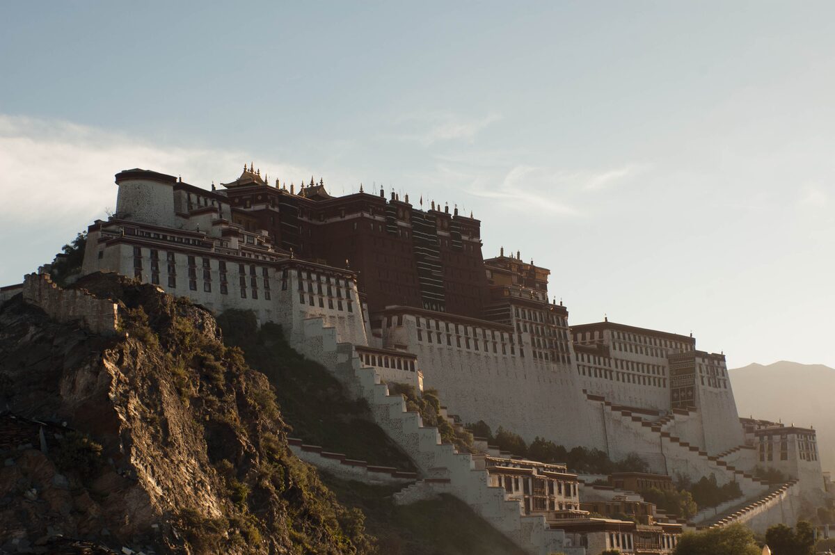 The Potala Palace on its rocky hill in low evening light, the red palace catching the sun above stepped white walls