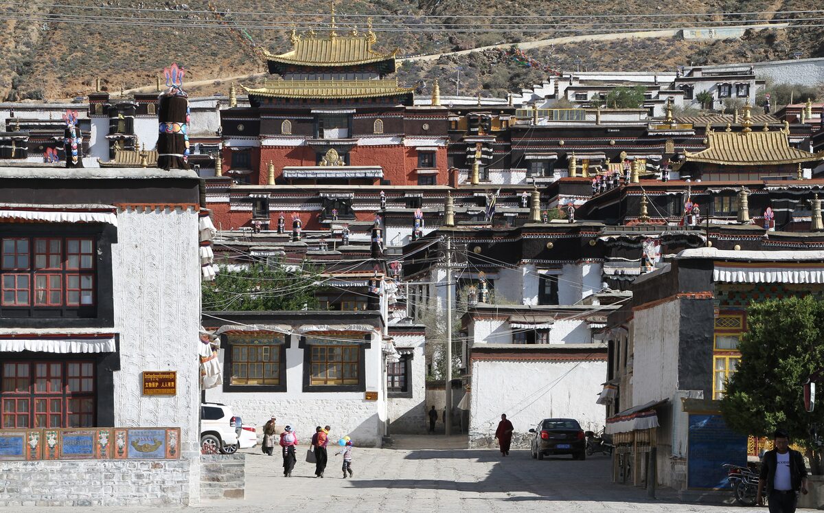 Tashilhunpo Monastery's whitewashed buildings and golden roofs packed on the hillside above a lane in Shigatse