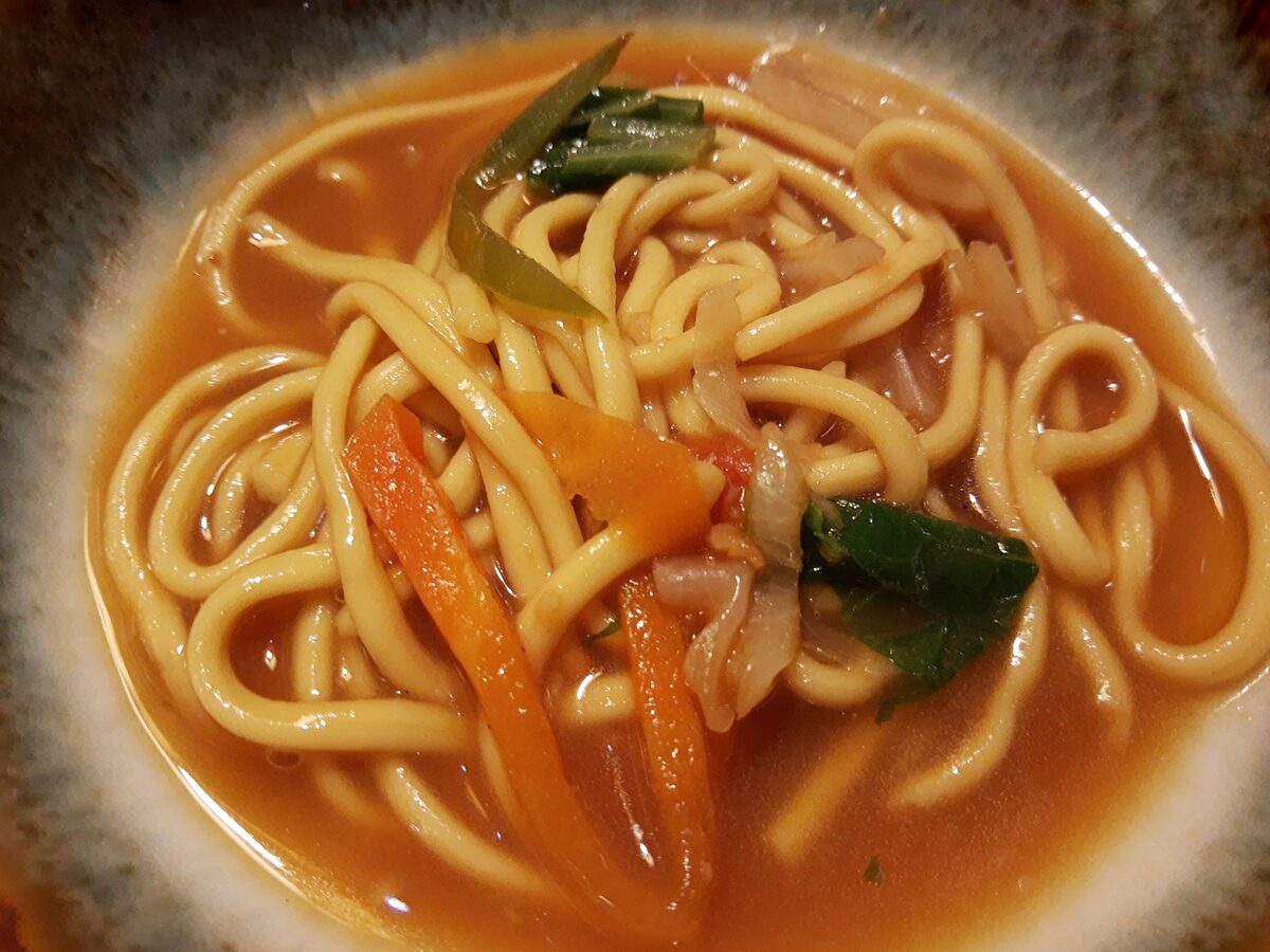 A bowl of thukpa, thick noodles with vegetables in an orange-red broth