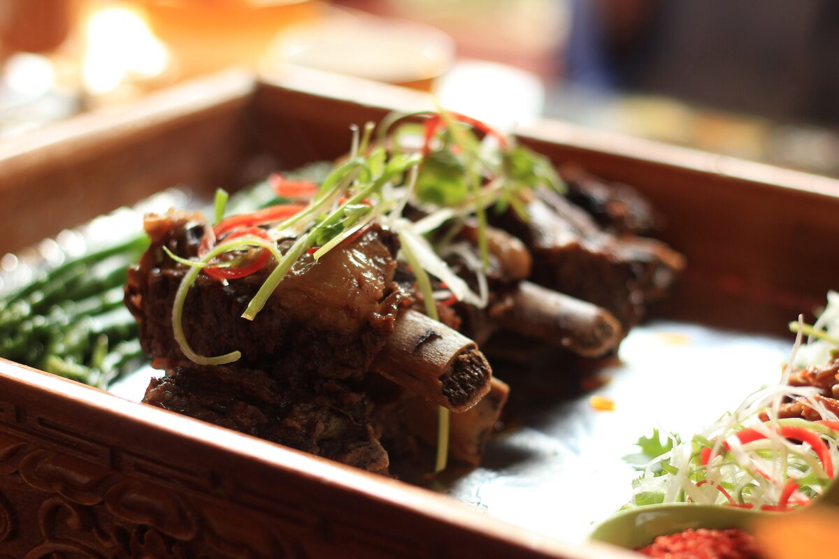 A glazed yak rib dish on a carved wooden tray with green beans and shredded vegetables