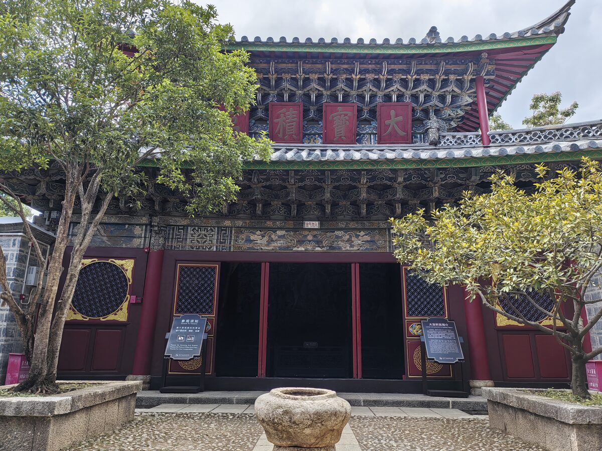 The carved and painted wooden front of the Dabaoji Palace in Baisha, with two small trees in the courtyard